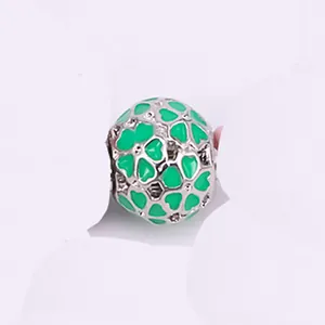 Macro shot of silver hollow charm featuring green enamel heart patterns for DIY bracelets