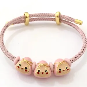 Primo piano di bracciale intrecciato rosa con ciondoli in smalto e chiusura dorata