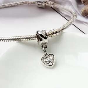 Detailed macro view of heart-shaped coin charm and snake chain bracelet on a plate