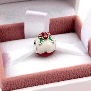 Macro shot of a festive Christmas holly enamel charm in a soft pink velvet jewelry box