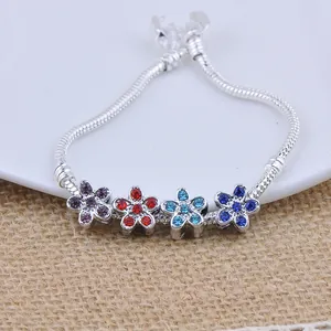 Silver snake chain bracelet with four colorful crystal flower charms on rustic background