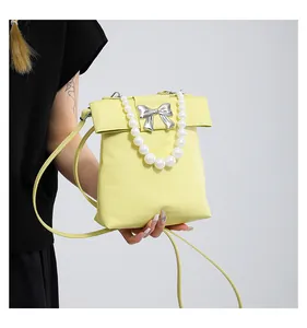 Detail of lemon yellow crossbody bag featuring a silver bow and pearl bead handle