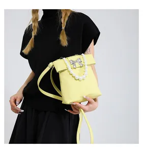 Detail of yellow crossbody bag featuring a silver bow buckle and large pearl handle