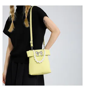 Detail of lime yellow handbag with white pearls and a silver metal bow accent