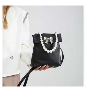 Detail of elegant black matte leather bag with white pearl handle and bow accent