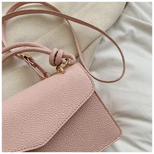 Detail of pink pebbled leather crossbody bag featuring gold hardware and knotted strap