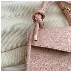 Detailed macro view of pink litchi grain leather bag featuring a knotted handle design