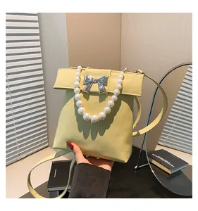 Detailed view of yellow handbag with silver bow, pearl handle, and leather strap