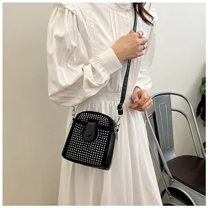 Detail of a mini crossbody bag with silver studs worn over a white elegant dress