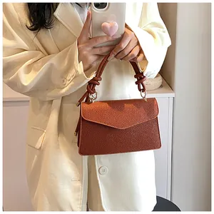 Detail of a brown lychee pattern leather handbag with a knotted handle and golden rings
