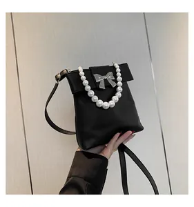 Detail of black mini crossbody bag featuring a silver bow and oversized pearl handle