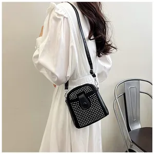 Detail of a black crossbody bag with silver studs worn by a model in a white dress