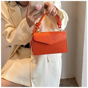 Detail of orange leather crossbody bag with chunky knotted handle and golden rings