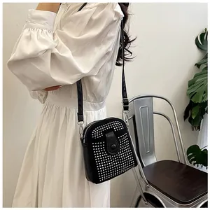 Detail of black crossbody bag with silver rivets worn over a white lace dress