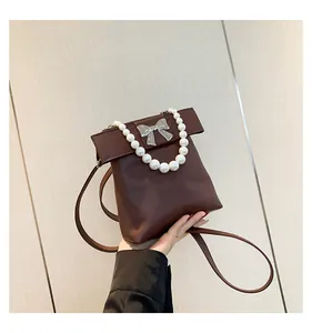 Detail of dark brown pearl handle bag with large bow design and thin shoulder strap