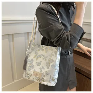Detail of blue butterfly embroidery and tassel on a stylish white shoulder bucket bag