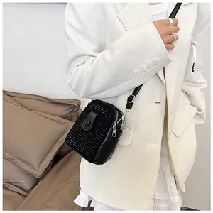 Detail of a mini black rhinestone crossbody phone bag with chain strap on white outfit