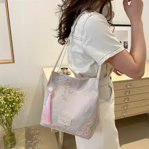 Pink satin tote bag with floral embroidery and tassel charm shown in a cozy interior