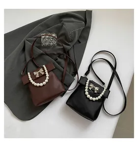 Detail of mini pearl handle crossbody bags with bow design in black and dark brown