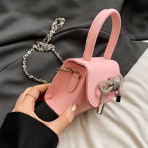 Detailopname van roze mini-handtas met strass-strik en zilveren kettingriem