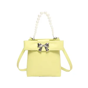 Elegant cream yellow mini bag with pearl handle and silver bow accent in front view