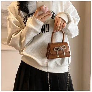 Detail van bruine mini-tas met litchi-patroon, strass strik en zilveren kettingriem