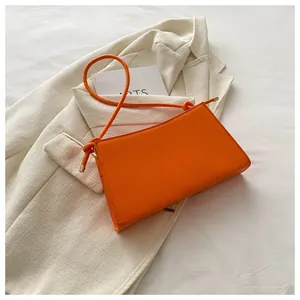 Dettaglio della borsa baguette arancione con tracolla annodata su sfondo blazer bianco