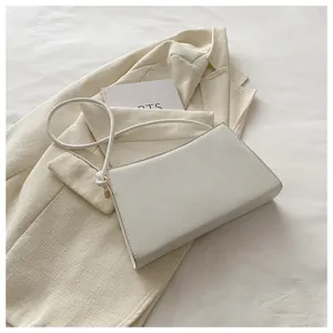 Dettaglio borsa sottobraccio bianco crema con tracolla annodata su blazer beige
