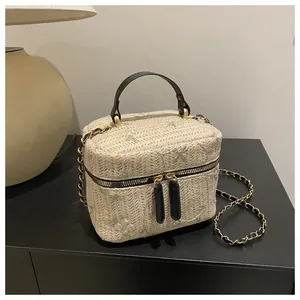 Detail of straw box bag with lace floral embroidery, gold chain, and black handle