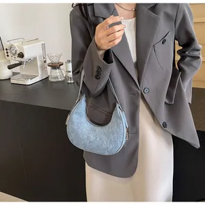 Close-up of a blue denim texture crescent hobo bag held by a model in a cafe