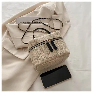 Close-up of beige straw box bag with floral embroidery and elegant gold chain strap
