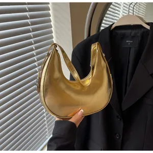 Detail of a shiny metallic gold crescent hobo bag with polished texture and silver buckle