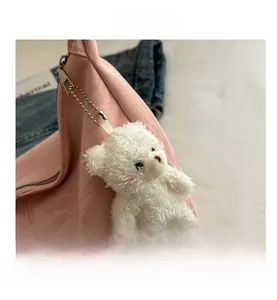 Close-up of a cute white plush bear charm with metal chain on a pink fashion handbag