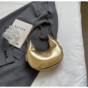 Detail shot of golden crescent shoulder bag with metallic finish on dark blazer background