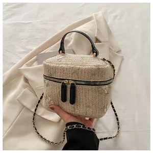 Detail of floral embroidery on a beige woven straw box bag with double zipper and gold hardware