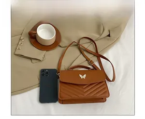 Close-up of brown V-quilted handbag with butterfly clasp next to smartphone for scale