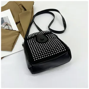 Detailed top view of black crossbody bag with silver studs on brown blazer backdrop