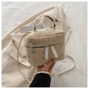 Detail of floral embroidery on beige straw bucket bag with gold chain strap
