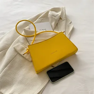 Elegante borsa baguette gialla con scritta Fashion accanto a uno smartphone per scala