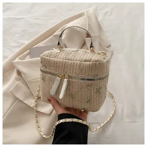 Close-up of woven straw box bag featuring green flower embroidery and golden chain strap