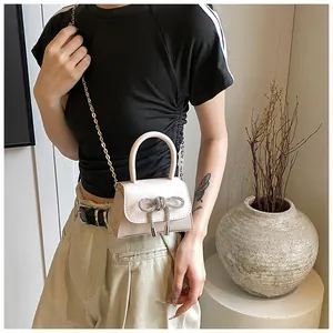 Detail van beige crossbodytas met strik van getextureerd leer en glanzende strass