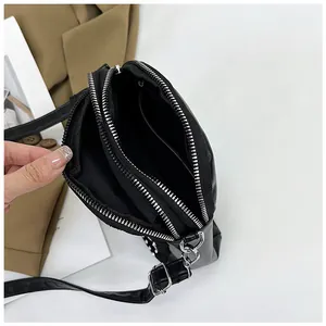 Detail view of the black crossbody bag showing three zippered compartments and silver hardware