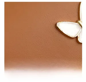 Detail of caramel leather texture and white butterfly metal emblem on stylish crossbody bag