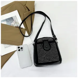 Detail of a black crossbody bag featuring silver rivet studs and a thin leather strap
