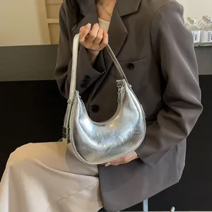 Chic silver metallic crescent hobo bag with pleated texture worn by a model in a suit
