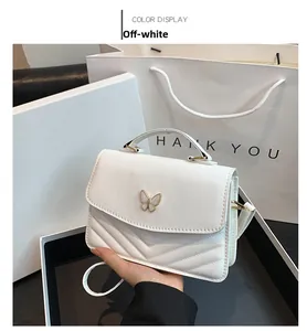 Detailed view of beige crossbody bag with V-shaped quilting and butterfly metal ornament