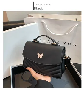 Detail view of a black fashion handbag featuring a white butterfly buckle and V-shaped quilting