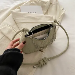 Olive green pleated underarm bag with silver chain and pearl charms on white blazer