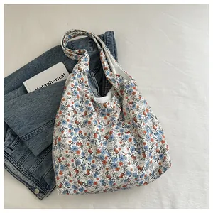 Detail of floral tote bag with blue and rust patterns on white fabric near a book