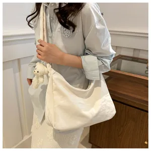 Detail of white large capacity tote bag with soft leather texture and bear pendant